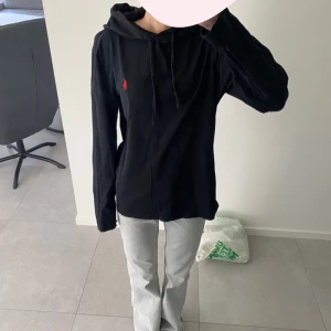 Svart hoodie från Polo Ralph Lauren - Tunn sart hoodie från Polo Ralph Lauren med röd broderad logga på bröstet. Tröjan har huva och långa ärmar. Perfekt för en avslappnad och stilren look.