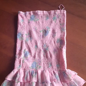 Rosa blommig kjol från Bik Bok - Charmig rosa kjol från Bik Bok med blommigt mönster. Kjolen har en volangdetalj längst ner och är elastisk för en bekväm passform. Perfekt för en somrig look!