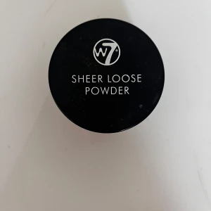 W7 Sheer Loose Powder - Transparant löspuder från W7 i en rund burk med svart lock. Perfekt för att fixera sminket och ge en matt finish. Pudret är ljust och passar de flesta hudtoner. Enkel att applicera med borste eller puff.
