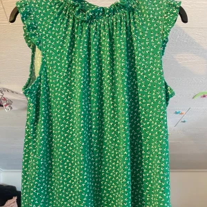 Grön blommig klänning från Adrianna Papell - Säljer en grön ärmlös klänning från Adrianna Papell med små vita blommor. Klänningen har rynkad halsringning och volangdetaljer vid axlarna. Perfekt för sommarens tillfällen!