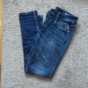 Blå Replay Anbass jeans - Storlek 33/32i slim. Jätte fint skick. Säljer ett par blå Replay Anbass jeans med snyggt slitna detaljer och klassisk femficksdesign. Jeansen har normal passform och raka ben, perfekt för en avslappnad stil. Märkeslapp bak i midjan och dragkedjegylf. Nya 2300. Nästan oanvända!
