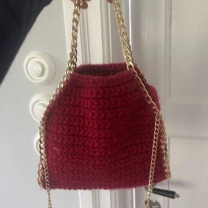 Röd virkad axelväska med guldkedja - Säljer en snygg röd virkad axelväska med lång guldfärgad kedja. Väskan har en mjuk och rymlig form, perfekt för att bära det viktigaste. Kedjan ger en lyxig touch och väskan är ett riktigt statement-piece. Jag köpte denna väska av en tjej som virkade den själv och den är väldigt skön att ta med till olika ställen. Aldrig använt. Köpte för 550kr. Stella McCartney liknande väska.