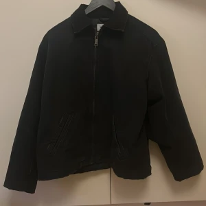 Svart manchesterjacka från Weekday - Säljer en svart manchesterjacka från Weekday med dragkedja framtill och klassisk krage. Jackan har två snedställda fickor och är perfekt för dig som gillar en stilren look. Endast använd en gång säljer pågrund av att den är för liten