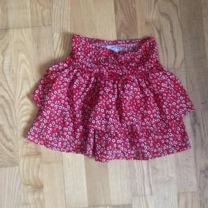 Röd blommig volangkjol - Supersöt röd kjol från Zara med små vita blommor och volanger. Kjolen har en smockad midja som gör den bekväm och sitter snyggt. 