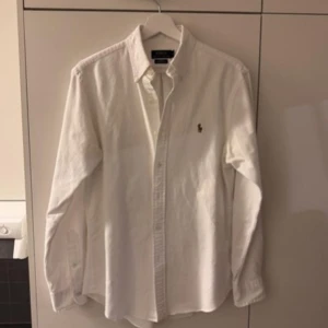 Vit skjorta från Ralph Lauren - Klassisk vit skjorta från Ralph Lauren med broderad logga på bröstet. Skjortan har lång ärm, knappar framtill och ett toppen plagg till sommaren! 