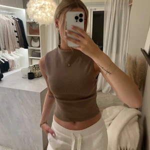 Beige ärmlös topp från Zara - Säljer en stilren beige ärmlös topp från Zara. Perfekt för lager-på-lager eller att bära som den är. Toppen har en mjuk och bekväm passform.