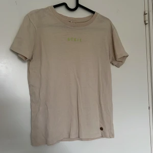 Beige t-shirt med tryck från Kappahl - Beige t-shirt med grön text ”rükie” använd fåtal gånger storlek 146/152🤍