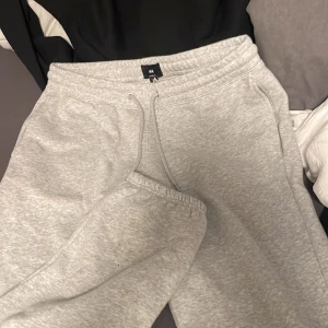 Grå mjukisbyxor från H&M - Säljer ett par grå mjukisbyxor från H&M i loose fit-modell. Byxorna har resår och snörning i midjan samt muddar vid bensluten. Perfekta för en avslappnad stil och riktigt sköna att ha på sig.