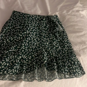 Grön blommig omlottkjol från SHEIN - Supersöt grön kortkjol från SHEIN med vitt blommönster och volangdetalj. Kjolen har omlottmodell och är perfekt för dig som gillar en feminin och trendig stil. Lätt och luftig, passar perfekt till varma dagar.