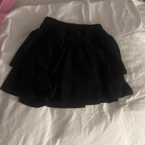 Svart volangkjol från SHEIN - Säljer en svart kjol från SHEIN med volangdetaljer och elastisk midja. Kjolen har en kort modell och är perfekt för dig som gillar en lekfull och trendig stil.