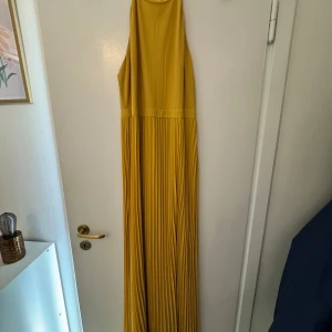 Gul långklänning med spetsdetalj - Säljer en gul långklänning med plisserad kjol och vacker spets i ryggen. Använd en gång 💛