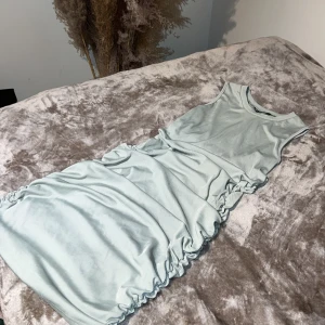 Ljusblå ärmlös klänning - Snygg ljusblå ärmlös klänning med rynkade detaljer längs sidorna. Perfekt för en stilren look. Klänningen har en kort längd och är tillverkad i ett mjukt material.