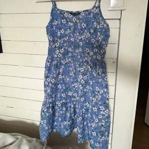 Blå blommig klänning från Shein - Säljer en fin och söt blå klänning från Shein med blommigt mönster. Klänningen har smala axelband och knappar framtill. Perfekt för sommarens alla tillfällen! 🌸