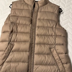 Beige dunväst från Vila - Snygg beige dunväst från Vila med dragkedja framtill. Perfekt för lager-på-lager under kyliga dagar. Västen har en quiltad design och är både stilren och praktisk.