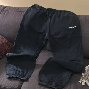 Svarta mjukisbyxor från Champion - Säljer ett par svarta mjukisbyxor från Champion. Byxorna har en elastisk midja med dragsko och resår vid bensluten. Perfekta för en avslappnad stil.