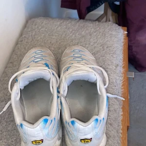 Vita och blå Nike sneakers - Säljer ett par vita Nike sneakers med blå detaljer och snörning. Skorna har en sportig design med synlig Nike-logga på sidan och en bekväm passform.