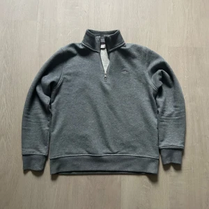 Grå tröja med dragkedja från GANT - Säljer en stilren grå tröja från GANT med dragkedja vid halsen. Tröjan har långa ärmar och en bekväm passform. Storlek 158-164