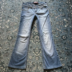 Blå bootcut jeans med broderade fickor - Snygga blå bootcut vintage jeans med broderade detaljer på bakfickorna. De har en klassisk femficksdesign och knäppning med dragkedja. Passar någon lite kortare ca 153-157 cm. Midjemått tvärsöver: 34 cm. Innerbenslängd: 70 cm.