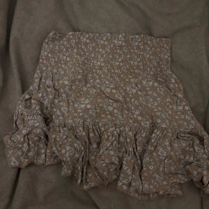 Beige blommig kjol - Charmig beige kjol med blommigt mönster och volanger. Perfekt för en somrig look med sin korta längd och elastiska midja.🥰