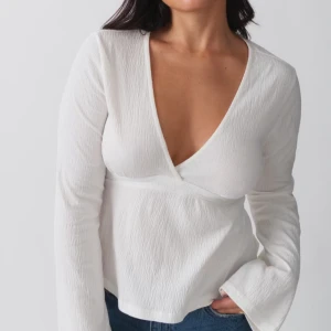 Vit omlottopp - Säljer en stilren vit omlottopp med v-ringning och långa ärmar. Toppen har en knytning i midjan som ger en fin passform. Perfekt för en chic och enkel look.