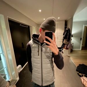 Grå dunväst från The North Face - Säljer en stilren grå dunväst från The North Face. Västen har dragkedja och flera praktiska fickor. Perfekt för lager-på-lager under kyligare dagar. 🧥