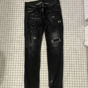 Svarta dsquare jeans  - Snygga svarta jeans med slitningar och en cool, sliten look. De har en dragkedja och knappar framtill. Perfekta för en trendig stil.  Skick: 7/10. Nypris: ca 5000. Mitt pris: 1300. Ej hugget i sten