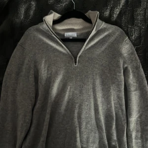 Grå kashmirtröja från Davida - Säljer en elegant grå kashmirtröja från Davida med dragkedja vid halsen. Tröjan har en stilren design och är perfekt för kyligare dagar. Den är tillverkad i 100% kashmir vilket gör den extra mjuk och bekväm. Passar perfekt för en stilren look.