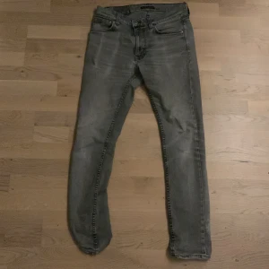 Grå jeans från Nudie Jeans Co - Snygga grå jeans från Nudie Jeans Co med en klassisk femficksdesign. De har en rak passform och är tillverkade i slitstarkt denim. Perfekta för en avslappnad stil.