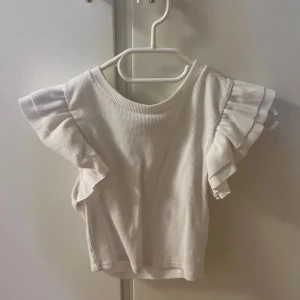 Vit ribbad topp med volangärmar - Säljer en söt vit ribbad topp med volangärmar. Perfekt för en somrig look med sin luftiga design och stilrena färg.