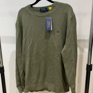 Ralph Lauren tröja stickad  - Helt ny och oanvänd stickad Ralph Lauren tröja, 10/10 skick. Färgen är oliv grön. Den har inga skador eller liknande, men den är lite skrynklig pga en flytt. Men de går lätt att lösa. Hör av er vid intresse!