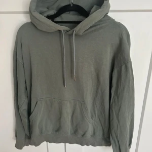 Grå hoodie med ficka - Säljer en stilren grå hoodie med en stor ficka framtill och justerbar huva. Perfekt för en avslappnad look. Passar bra till både jeans och mjukisbyxor.