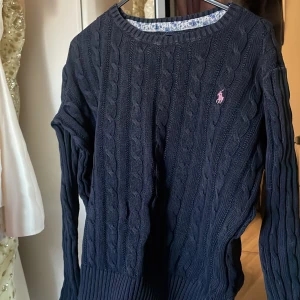 Mörkblå stickad tröja från Polo Ralph Lauren - Säljer en snygg mörkblå stickad tröja från Polo Ralph Lauren med kabelstickat mönster. Tröjan har långa ärmar och en liten rosa logga på bröstet. Perfekt för kyliga dagar! Har tyvärr blivit för liten på mig, därför säljer jag denna 💓💓