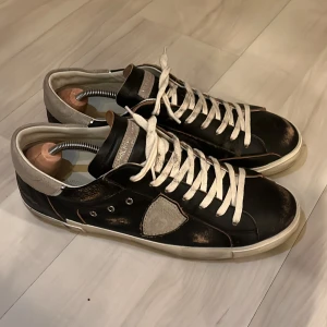 Brun Svarta sneakers från Philippe Model - Snygga brun svarta sneakers från Philippe Model med vita snören och detaljer i beige. Skorna har en unik design med en sliten look och en vit sula. Storlek 43. Perfekta för en stilren och avslappnad stil. Använda en gång. Säljes pga fel storlek för mig. Dustbag och låda följer med. Nypris omkring 3400kr. 