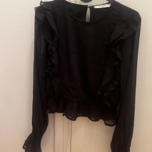 Svart blus från NA-KD - Snygg svart blus från NA-KD med volangdetaljer och långa ärmar.