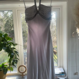 Ljusgrå långklänning med pärldetaljer - Jättefin balklänning endast använd 1 gång. Elegant ljusgrå långklänning med pärldetaljer vid bysten och halterneck-design.  