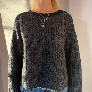 Mörkgrå stickad tröja - Säljer en mysig mörkgrå stickad tröja med rund hals och långa ärmar. Perfekt för kyliga dagar och enkel att matcha med jeans eller kjol. Tröjan har en ribbad struktur som ger en stilren look.
