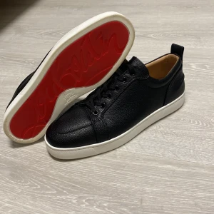  louboutin - Snygga svarta sneakers i skinn med den ikoniska röda sulan från Christian Louboutin. Skorna har en klassisk snörning och en vit sula som kontrasterar snyggt mot det svarta lädret. Perfekta för att ge din outfit en lyxig touch. Tvättar de även innan jag fraktar