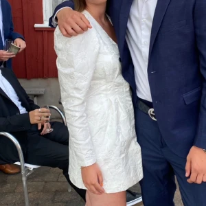 Vit klänning - Världens finaste vita klänning med blommigt mönster. Klänningen har en v-ringad design och långa puff ärmar, den är skräddarsydd i midjan så sitter otroligt fint på. Perfekt för studenten. Använd endast en gång. Den är som ny. Storlek 34 men passar även 36/s. Knappar framtill som inte syns. 