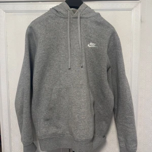 Grå hoodie från Nike - Säljer en klassisk grå hoodie från Nike med justerbar huva och känguruficka. Perfekt för en avslappnad stil. Den har en liten Nike-logga på bröstet och ribbade muddar vid ärmslut och nederkant.