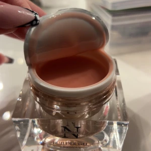 Builder Gel från Nagelexperten - Säljer en 30 ml burk med Builder Gel från Nagelexperten. Gelen har en fin nude/coral/orangd färg och kommer i en elegant förpackning med guldlock. Perfekt för att bygga starka och hållbara naglar med en naturlig look. Endast använd på en nagel.