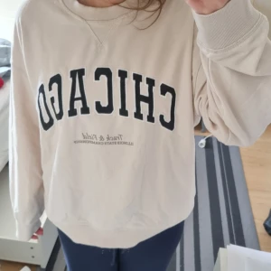 Beige sweatshirt med tryck  - En beige sweatshirt med texten 'CHICAGO Track & Field' tryckt på framsidan. Tröjan har långa ärmar och en rund halsringning. Från H&M. Nypris: 299 kr