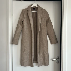Beige kappa från Zara - Säljer en stilren beige kappa från Zara. Den har en klassisk design med långa ärmar och är perfekt för höst och vår. Materialet känns mjukt och bekvämt. 