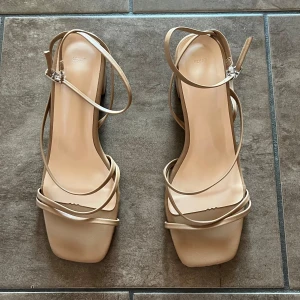 Beige sandaler med klack - Snygga beige sandaler med klack och smala remmar. De har en fyrkantig tå och justerbara spännen för perfekt passform. Perfekta för bal, student, fest eller till sommaren. Aldrig använda, normala i storleken.