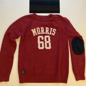 Röd tröja från Morris - Säljer en snygg röd tröja från Morris med texten 'Morris 68' i vitt på framsidan. Tröjan har långa ärmar och svarta armbågslappar som ger en cool touch. Perfekt för en avslappnad stil.