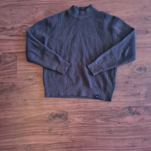 Grön ribbad tröja från Pull&Bear - Säljer en stilren grön ribbad tröja från Pull&Bear. Tröjan har en hög krage och långa ärmar, perfekt för kyligare dagar. Ser grå ut på bilderna men är mörkgrön. Knappt använd, så i princip helt ny