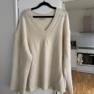 Vit stickad tröja från gina Tricot  - Säljer en mysig krämvit stickad tröja från Hina Tricot med v-ringning. Tröjan har långa ärmar och ribbade detaljer vid ärmslut och nederkant. 