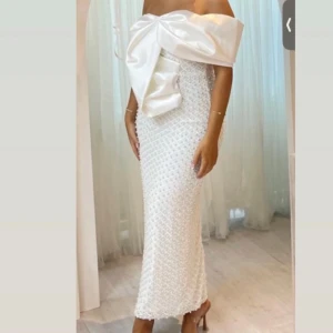 Vit axelbandslös klänning med stor rosett - Använd endast en gång på min förlovning, ren och utan skada. Jätte fin klänning med pärlor och paljetter, den har ett slit på baksidan av klänningen. 