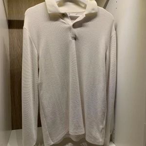 Långärmad pikétröja från H&M - Säljer en stilren vit/begie  långärmad pikétröja från H&M. Tröjan har en klassisk krage och knäppning framtill. Perfekt för en avslappnad men ändå snygg look. 