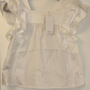 Vit blus med volanger  från MNG - Säljer en söt vit blus från MNG med volanger  längs axlarna. Perfekt för sommarn. Helt ny!!!🤍🤍💛 Stl 152 från MNG kids men passar mig som har xs-s i vanliga fall.