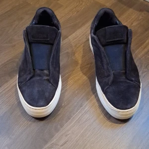 Svarta sneakers från Axel Arigato - Snygga svarta sneakers från Axel Arigato i mocka. Synligt slitna. Sömen har börjat lossna lite, men nog lätt att fixa. Kan hämtas i Hudiksvall eller skickas. Pris kan diskuteras